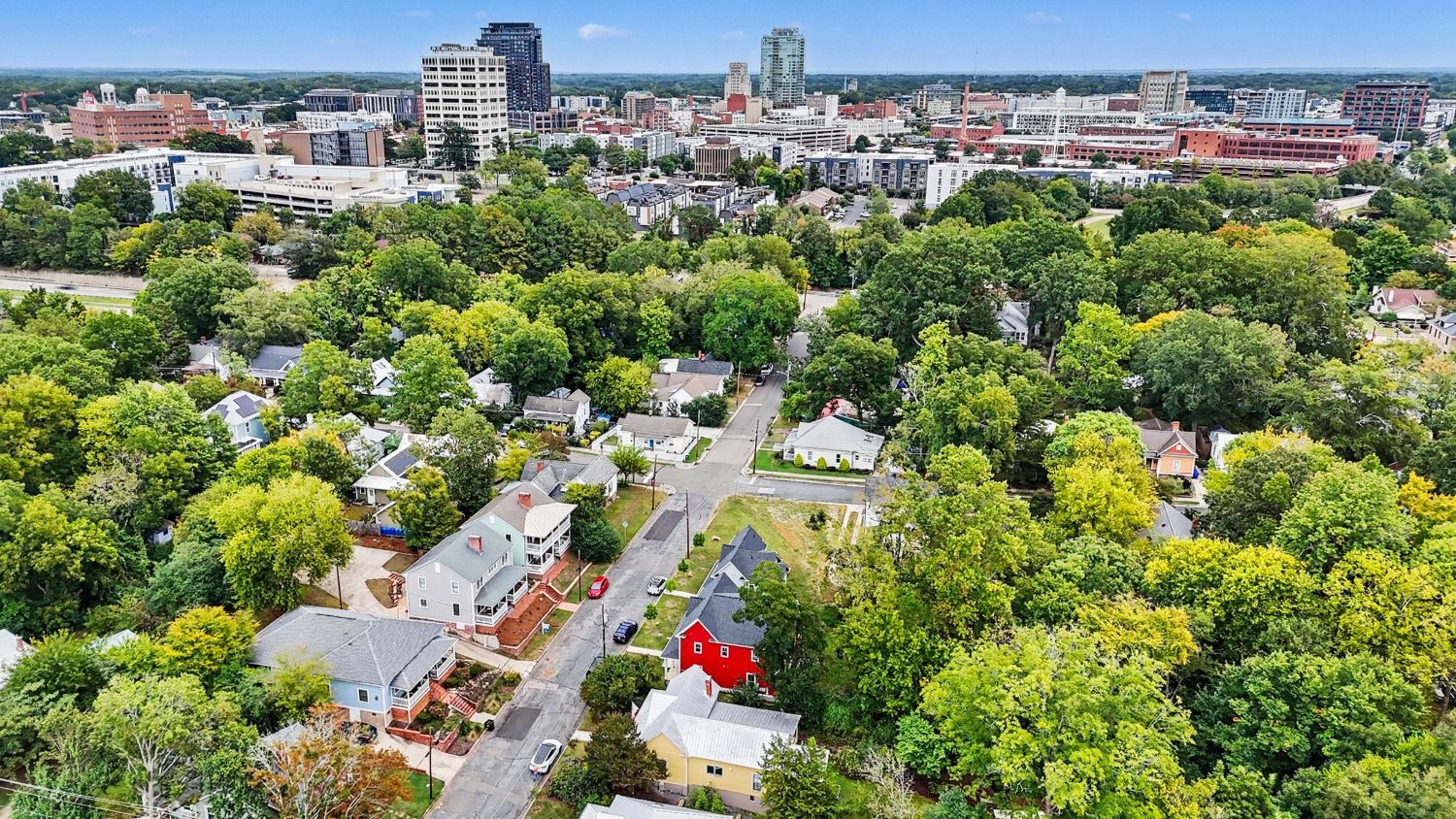 Aerial view of a tree-lined Raleigh neighborhood with the downtown skyline behind it