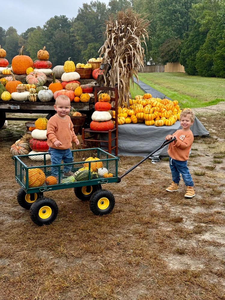 Two kids pulling a wagon full of pumpkins